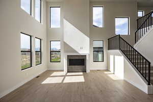 Unfurnished living room with a tile fireplace, a high ceiling, light wood finished floors, and stairway