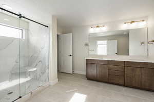 Bathroom featuring double vanity, a marble finish shower, light tile patterned flooring, and a textured ceiling