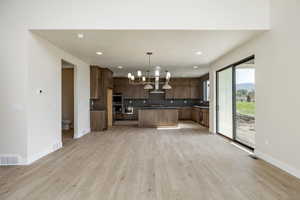 Kitchen with dark countertops, a chandelier, decorative light fixtures, light wood-style floors, and tasteful backsplash