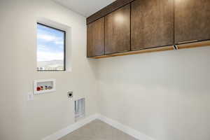 Washroom with light tile patterned floors, hookup for a washing machine, cabinet space, and electric dryer hookup