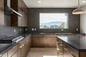 Kitchen with wall chimney range hood, a mountain view, backsplash, light wood-type flooring, and decorative light fixtures