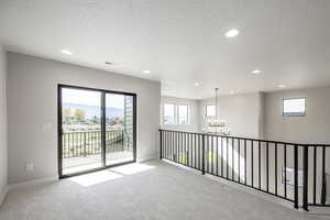 Unfurnished room featuring light carpet, plenty of natural light, a textured ceiling, recessed lighting, and a chandelier