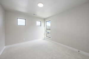 Empty room with light carpet and a textured ceiling