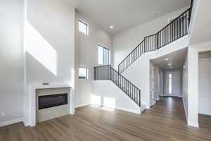 Unfurnished living room with a towering ceiling, a glass covered fireplace, recessed lighting, light wood-style flooring, and stairway