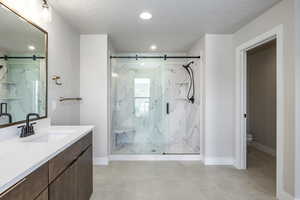 Bathroom with a textured ceiling, vanity, and a marble finish shower
