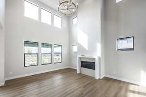 Unfurnished living room featuring a glass covered fireplace, a towering ceiling, wood finished floors, and a chandelier
