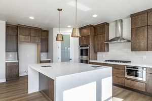 Kitchen with backsplash, a center island, light wood-type flooring, wall chimney range hood, and a textured ceiling
