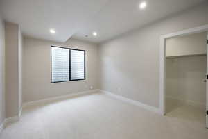Unfurnished bedroom featuring light colored carpet, a walk in closet, and recessed lighting