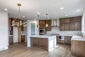 Kitchen featuring decorative backsplash, a center island, wall chimney exhaust hood, light stone counters, and light wood-style flooring