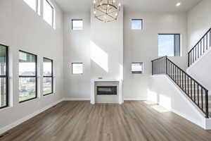 Unfurnished living room with healthy amount of natural light, wood finished floors, a towering ceiling, a glass covered fireplace, and stairway