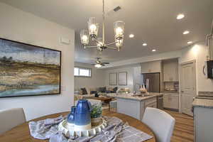 Dining room with visible vents, light wood finished floors, recessed lighting, and ceiling fan with notable chandelier