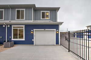 View of front of home featuring central AC, a garage, board and batten siding, fence, and driveway