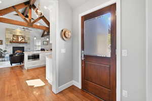 Foyer entrance with baseboards, a stone fireplace, a ceiling fan, light wood-style flooring, and vaulted ceiling with beams