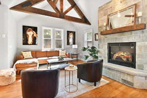 Living area with high vaulted ceiling, a stone fireplace, wood finished floors, baseboards, and beam ceiling