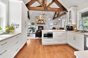 Kitchen featuring lofted ceiling with beams, a fireplace, a ceiling fan, light wood-style floors, and a sink