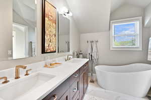 Bathroom featuring a freestanding tub, double vanity, a sink, and vaulted ceiling