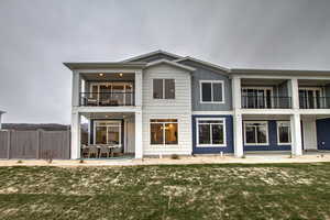 Back of property featuring a patio, a balcony, fence, and a lawn