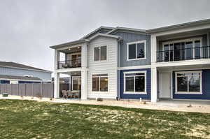 Back of house with a patio, a balcony, board and batten siding, a yard, and fence