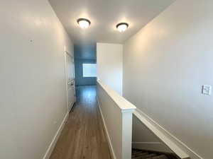 Hallway with wood finished floors, baseboards, and an upstairs landing