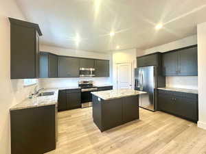 Kitchen with a center island, a sink, appliances with stainless steel finishes, light wood-style flooring, and light stone counters