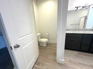 Full bathroom featuring toilet, vanity, wood finished floors, and baseboards
