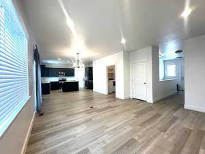 Unfurnished living room featuring baseboards, recessed lighting, an inviting chandelier, and light wood-style floors