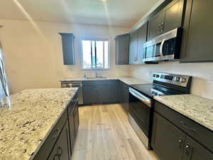 Kitchen with light wood-style floors, appliances with stainless steel finishes, a sink, and light stone counters