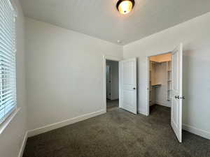 Unfurnished bedroom with dark colored carpet, multiple windows, and baseboards