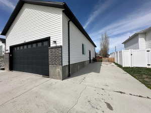 View of side of home featuring a garage, brick siding, fence, a gate, and driveway