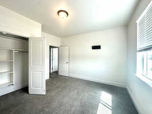 Unfurnished bedroom with dark carpet, baseboards, and a closet