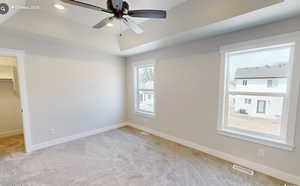 Unfurnished bedroom featuring visible vents, baseboards, a tray ceiling, carpet floors, and a walk in closet