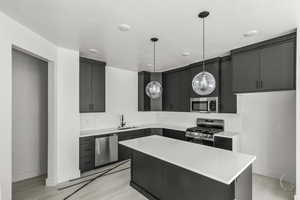 Kitchen featuring dark cabinets, stainless steel appliances, light countertops, a sink, and pendant lighting