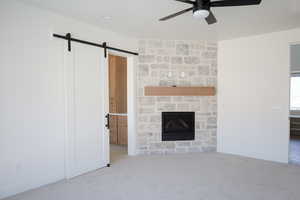 Unfurnished living room with a barn door, baseboards, a fireplace, carpet flooring, and ceiling fan