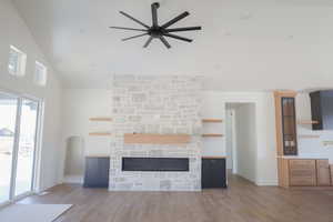 Unfurnished living room featuring wood finished floors, a healthy amount of sunlight, a ceiling fan, and high vaulted ceiling