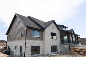 View of side of home with roof with shingles, board and batten siding, stone siding, and central AC unit