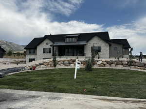 Modern farmhouse style home featuring stone siding, a front yard, a metal roof, and a porch