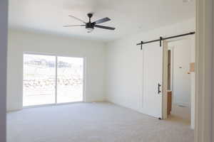 Carpeted spare room featuring a barn door, a ceiling fan, and baseboards