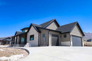 View of front facade with concrete driveway, board and batten siding, stone siding, a garage, and a shingled roof