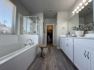 Bathroom featuring visible vents, a shower stall, double vanity, and wood finished floors