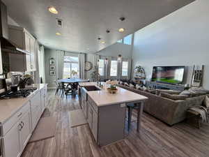 Kitchen featuring open floor plan, stainless steel gas stovetop, wall chimney exhaust hood, and visible vents