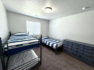 Bedroom with dark carpet, a textured ceiling, and visible vents