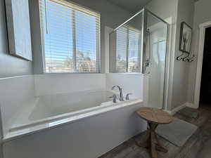 Full bath featuring plenty of natural light, a garden tub, a stall shower, and wood finished floors