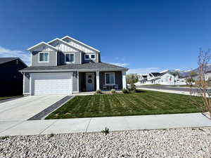 View of front of property with covered porch, a front lawn, an attached garage, a shingled roof, and concrete driveway