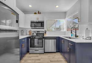 Kitchen featuring light wood-type flooring, blue cabinets, light countertops, a sink, and stainless steel appliances