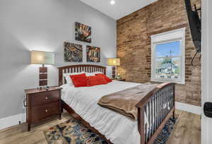 Bedroom featuring brick wall, wood finished floors, baseboards, and recessed lighting