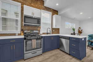 Kitchen with a peninsula, blue cabinets, light countertops, appliances with stainless steel finishes, and a sink