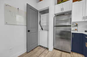 Laundry area with light wood-type flooring, baseboards, laundry area, and stacked washer and clothes dryer