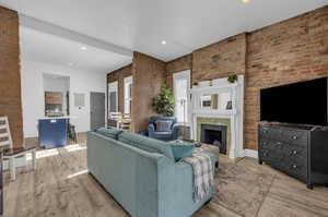 Living room featuring light wood-style flooring, recessed lighting, brick wall, and a fireplace