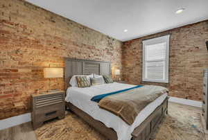 Bedroom featuring brick wall, light wood finished floors, and baseboards