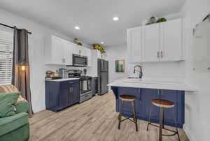 Kitchen with a sink, light countertops, white cabinetry, stainless steel appliances, and a breakfast bar area